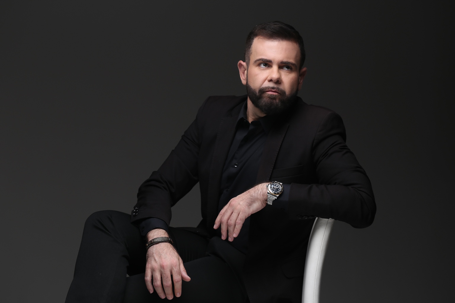 Lucas Atanazio sentado, de fato preto, num retrato horizontal de estúdio.
